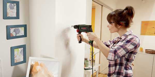 A woman drilling a hole with a hand drill in a wall.